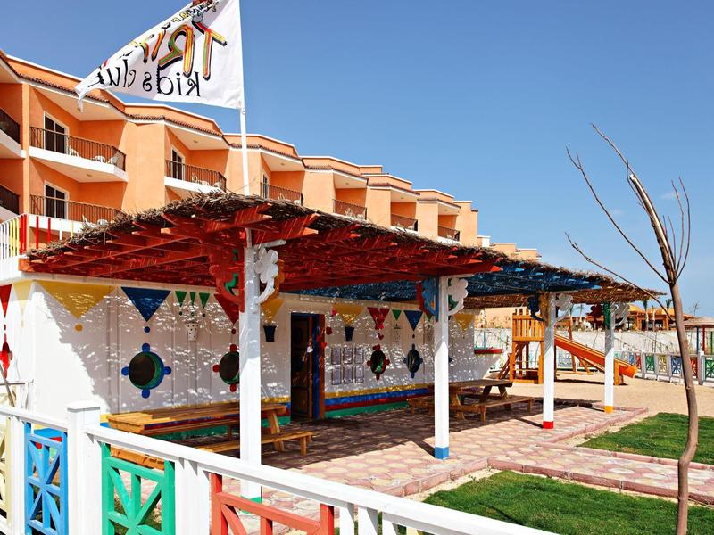 Hotelterrasse mit buntem Geländer, überdachtem Sitzbereich und sonnigem Garten.