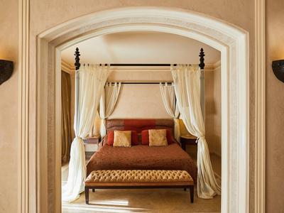 Elegant bedroom with four-poster canopy bed, brown bedding, and cushioned bench under archway