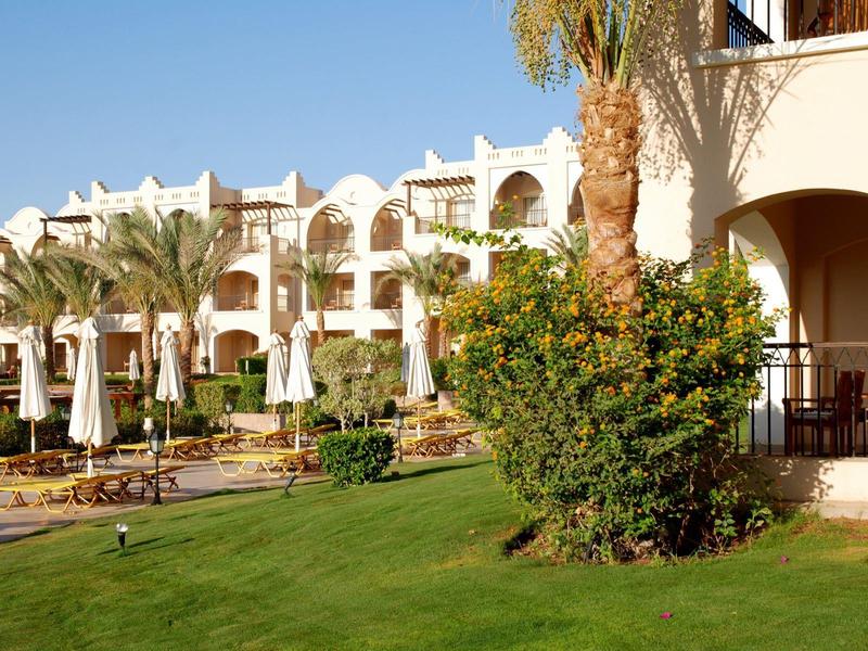 Hotel building with arched windows, palm trees, and green lawn in sunny weather.