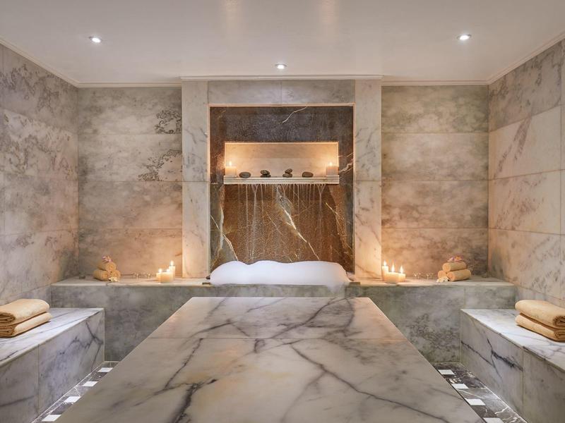 Luxurious marble bathroom with spa tub, soft lighting, and wooden towels on side benches.