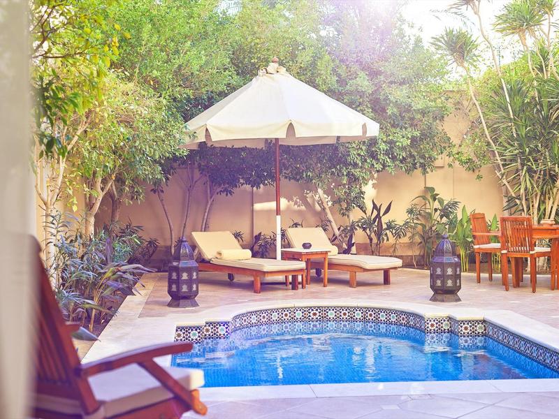 Peaceful patio with pool, lounge chairs, umbrella, and greenery in a cozy outdoor setting.