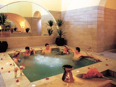 Innen-Jacuzzi mit sechs Personen, beige Fliesen, großen Spiegeln und grünen Pflanzen.