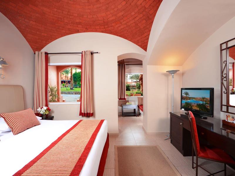 Gemütliches Schlafzimmer mit rotem Tonnengewölbe, großem Bett, Schreibtisch und Fenster mit Blick in Garten.