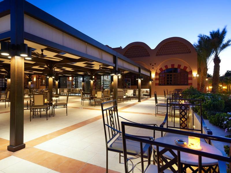 Abendliche Terrasse eines Hotels mit gedeckten Tischen und Gebäuden bei Sonnenuntergang.