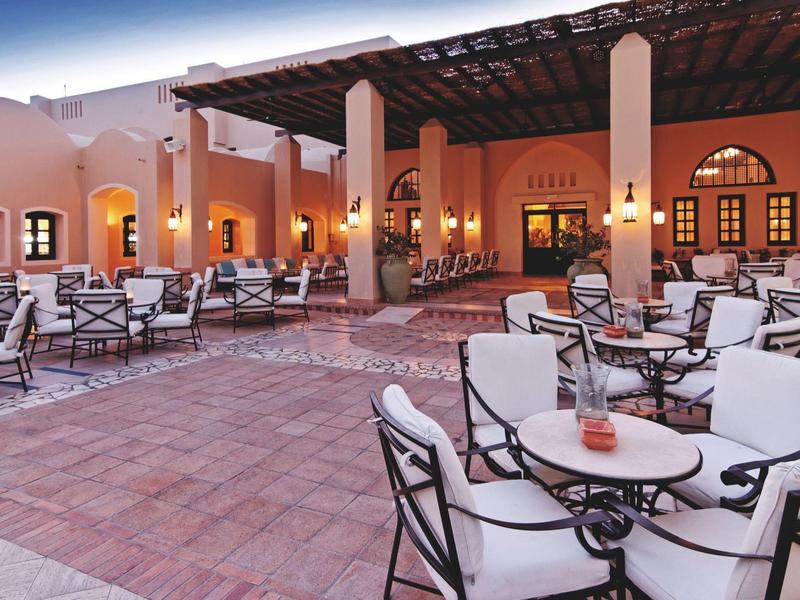 Außenbereich eines Hotels mit gepolsterten Stühlen und Tischen auf einer Terrasse bei Dämmerung.