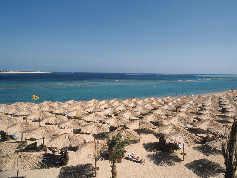 Strand mit vielen Sonnenschirmen aus Stroh und klarem blauem Himmel im Hintergrund.