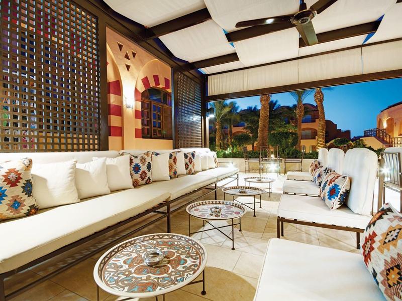 Moderner Lounge-Bereich mit weißen Sofas, bunten Kissen und runden Tischen auf hellen Fliesen.