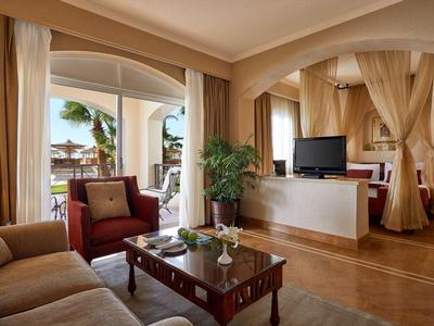 Gemütliches Wohnzimmer mit roten Sesseln, Holztisch, Pflanzen und Blick auf Meer und Palme.
