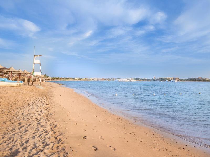 Sandstrand mit ruhigem Meer, blauem Himmel und wenigen Wolken, an einem sonnigen Tag.
