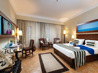 Bright hotel room with large bed, wooden furniture, and a seating area near window.