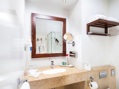 Bright bathroom with large mirror, beige countertop, white walls, and wooden shelf.