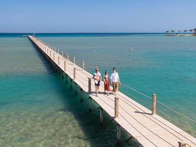 Lange houten pier strekt zich uit in de heldere blauwe zee met drie mensen die lopen.
