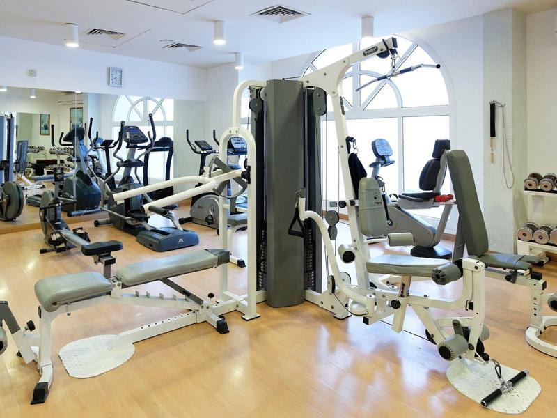 Bright gym with cardio and strength machines and large mirrors on the walls.