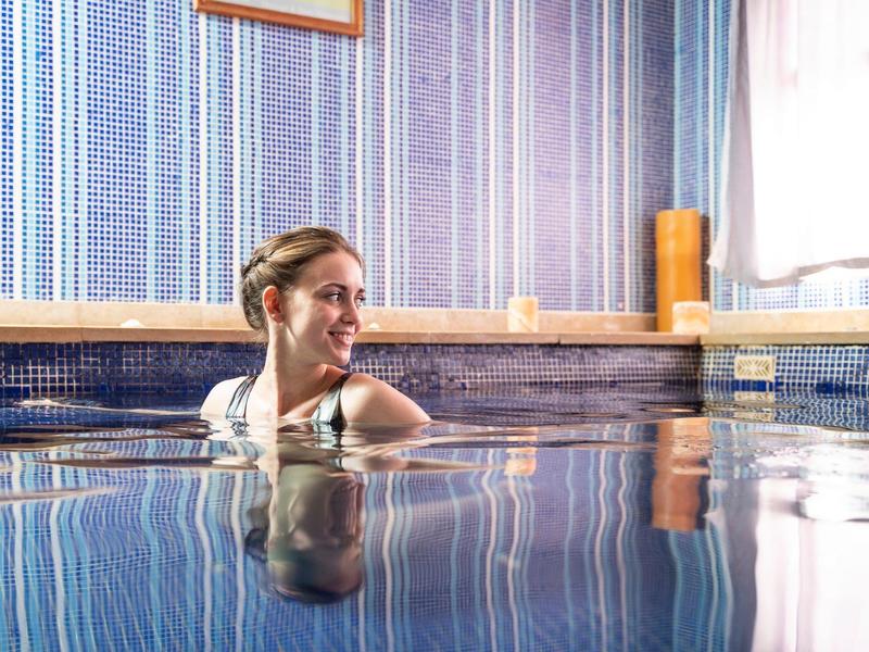 Woman relaxing in an indoor pool surrounded by blue-striped walls and a framed picture.