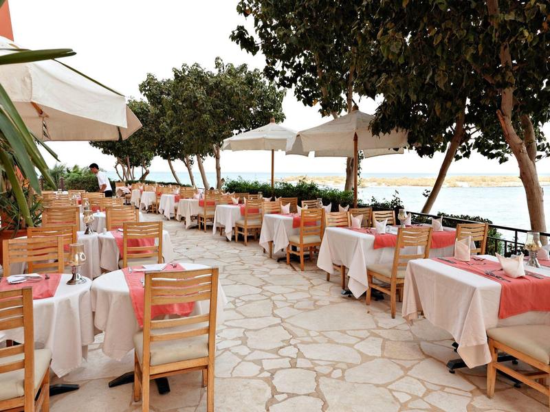 Outdoor restaurant with tables and chairs lined along a stone path by the sea.