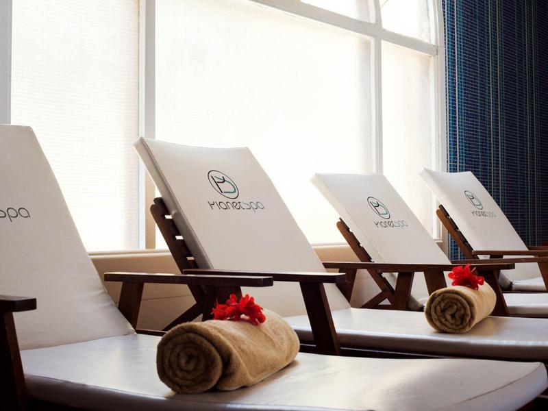 Spa lounge chairs with rolled towels and red flowers near a large window with curtains.