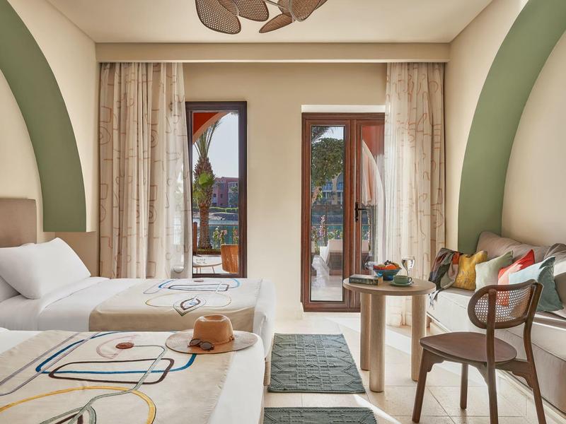 Hotel room with two beds, balcony doors, and seating area with chairs and table.