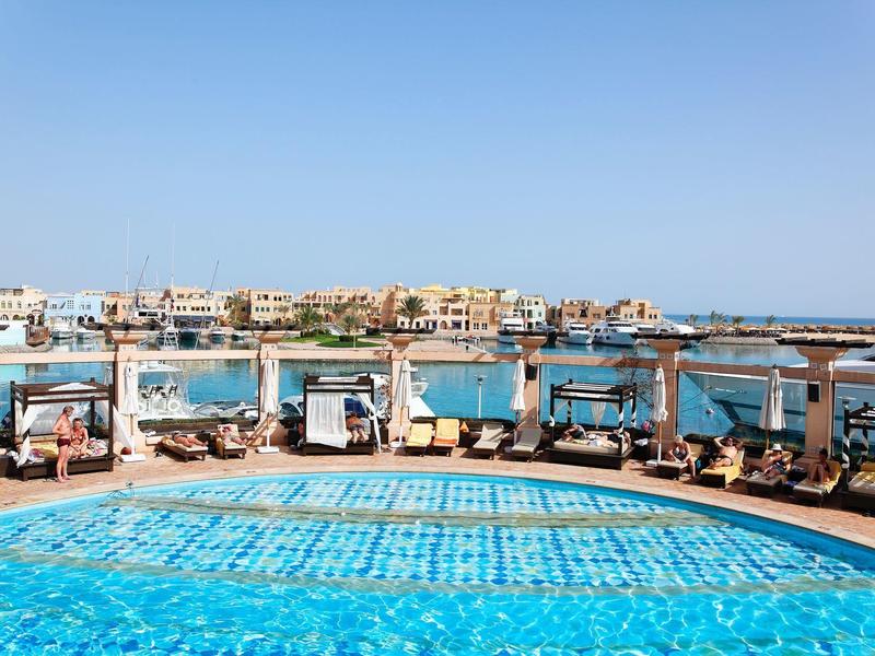 Outdoor pool with sunbeds and cabanas overlooking the sea under a clear blue sky.