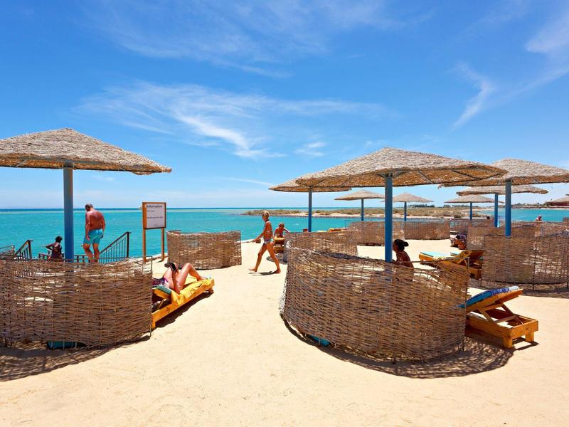 Beach with wicker umbrellas and lounge chairs under a clear blue sky.