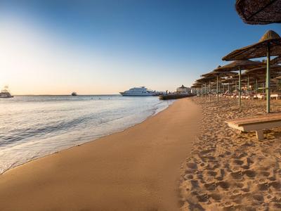 Beach at sunset with loungers and umbrellas along the water and cruise ships on the horizon.