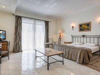 Helles Hotelzimmer mit Doppelbett, Glastisch, Schreibtisch, Fernseher und großen Fenstern mit Vorhängen.