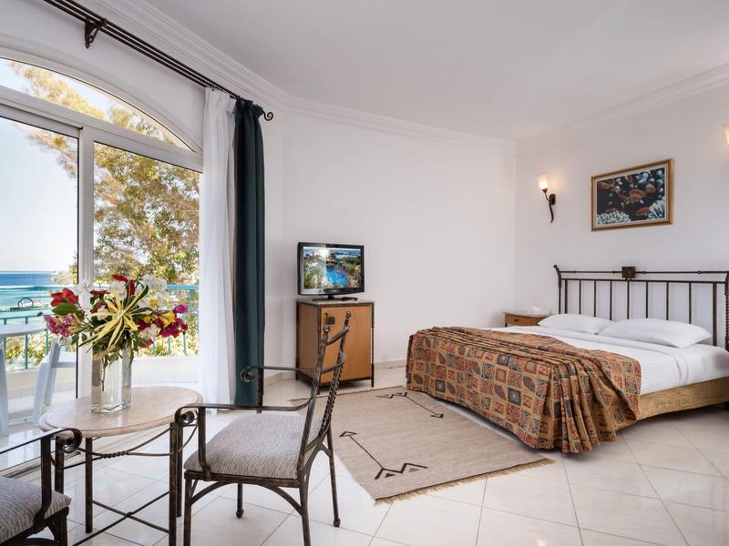 Hell eingerichtetes Schlafzimmer mit Doppelbett, Sesseln, Balkon und Meerblick.