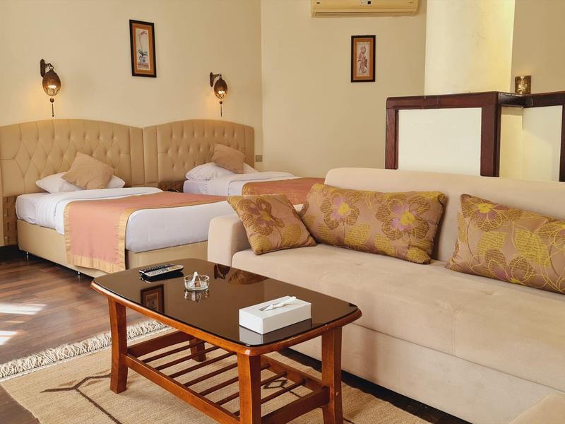 Helles Wohnzimmer mit Sofa, Holztisch und Doppelbett, neutralen Farben und warmem Tageslicht.