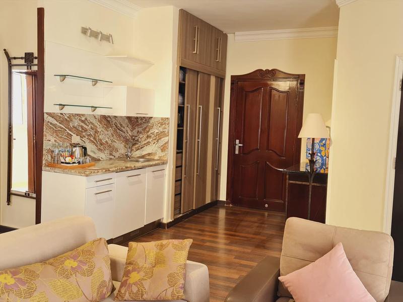 Gemütliches Wohnzimmer mit Sofa, Küchenzeile, Holzfußboden und zwei Türen aus dunklem Holz.