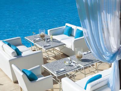 Modernes weißes Sofa-Set mit blauen Kissen neben blauem Wasser unter weißem Vorhang.