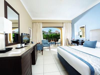 Helles Hotelzimmer mit großem Bett, Fernseher, Sesseln und Balkon mit Blick ins Grüne.