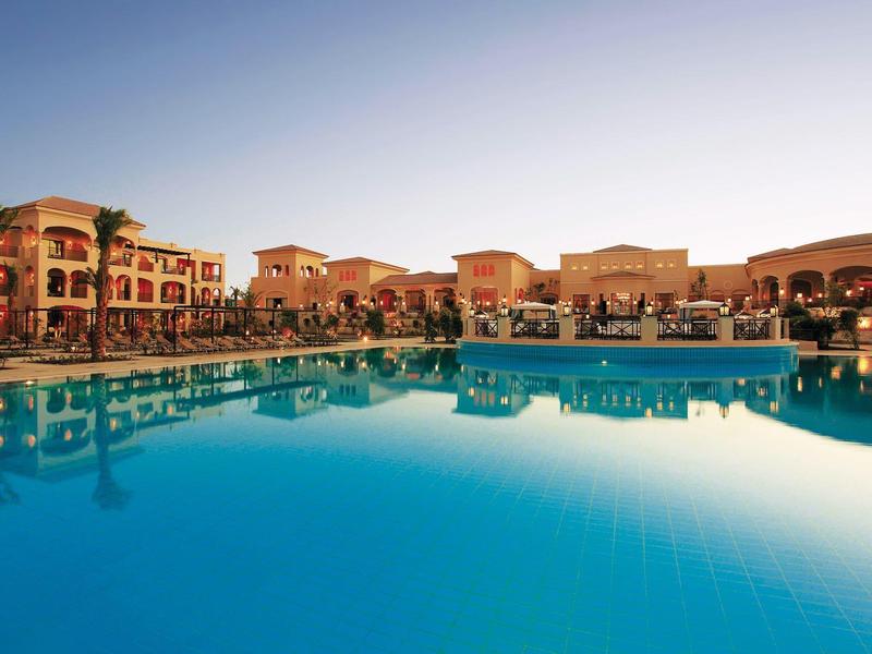 Großer, blauer Pool spiegelt orangefarbene Gebäude und klares Abendlicht wider.