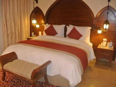 Gemütliches Hotelzimmer mit großem Bett, gepolstertem Hocker und warmem Licht an Holzwänden.