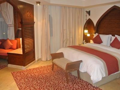 Gemütliches Hotelzimmer mit großem Bett, roten Kissen, Teppich und Sitzecke mit Sofa.