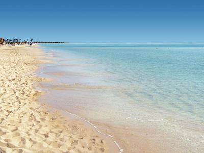 Piaszczysta plaża z czystą, spokojną wodą pod niebieskim niebem i parasolami w tle.