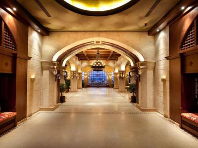 Duży korytarz hotelowy z marmurowymi łukami, eleganckimi ławkami i ciepłym oświetleniem.