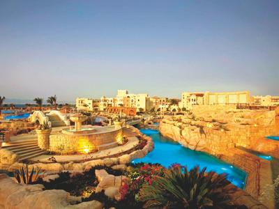 Hotelanlage mit Pool, umliegenden Felsen und Gebäuden bei klarem Himmel am Abend.