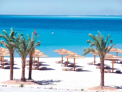 Terrasse mit blauen Stühlen und weißen Tischen, Palmen im Hintergrund, Meer und Berge sichtbar.