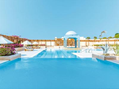 Großer blau schimmernder Pool mit weißer Poolinsel und Sonnenschirmen bei klarem Himmel.