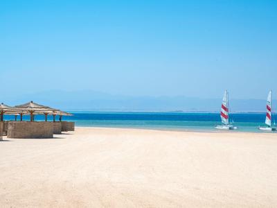 Plaża z piaskiem, parasolami i żaglówkami pod czystym niebieskim niebem i morzem.