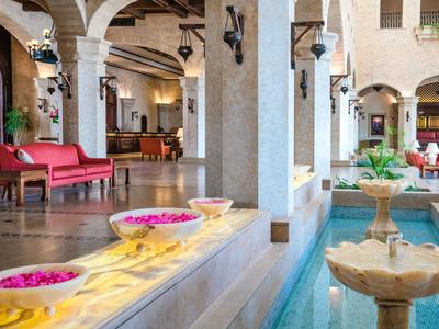 Elegancki hotelowy dziedziniec z kolumnami, fontannami i czerwonymi sofami pod drewnianym sufitem z belek.