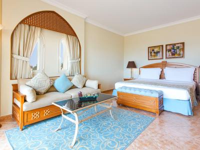 Elegancki pokój hotelowy z dużym łóżkiem, sofą, szklanym biurkiem i jasnoniebieskim dywanem.