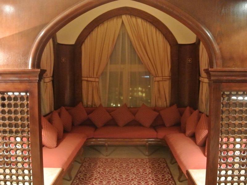 Gemütliche Sitzecke mit roten Kissen, Teppich und Vorhängen in warmem Holzbogen eingerahmt.