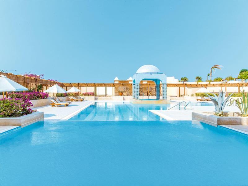 Großer blau schimmernder Pool mit weißer Poolinsel und Sonnenschirmen bei klarem Himmel.