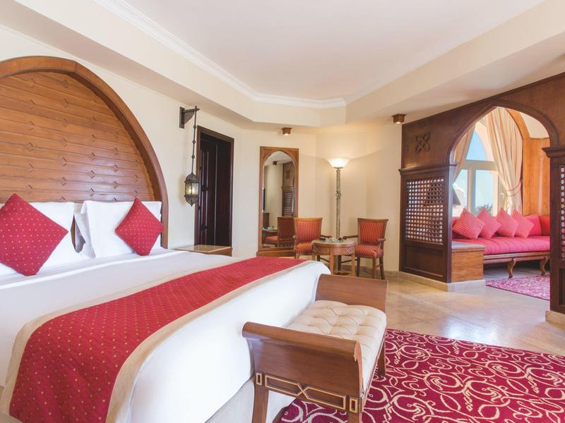 Elegantes Hotelzimmer mit großem Bett, roten Akzenten und Sitzbereich bei Tageslicht.