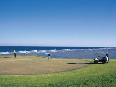 Dva golfisté hrají na golfovém hřišti poblíž moře za jasné modré oblohy.