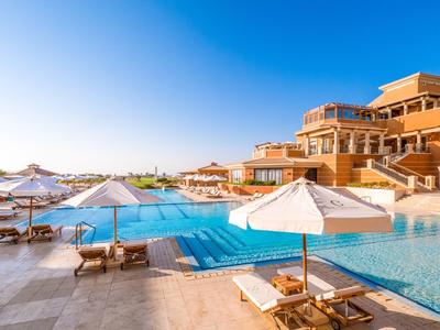 Luxusní hotelový bazén s lehátky a slunečníky pod jasně modrou oblohou.