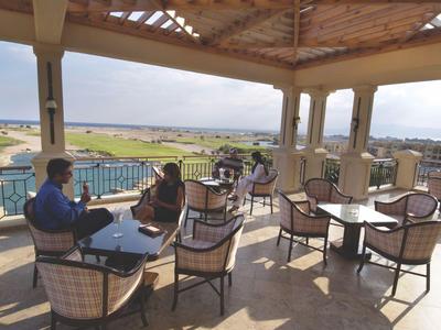 Zastřešená terasa s posezením a výhledem na bazén a zahradu za slunečného počasí.