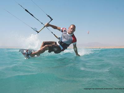 Muž kitesurfing na modrém moři pod jasnou oblohou.