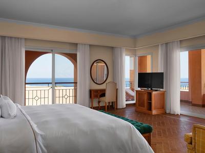 Bright hotel room with bed, balcony, and sea view through large windows.
