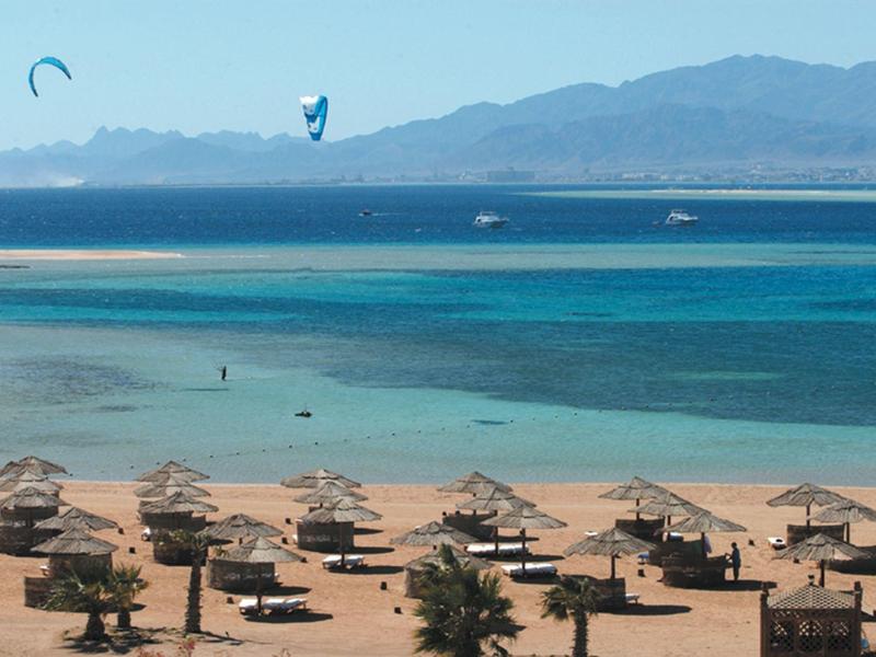 Beach with umbrellas and blue sea, mountains and kite surfers in the background